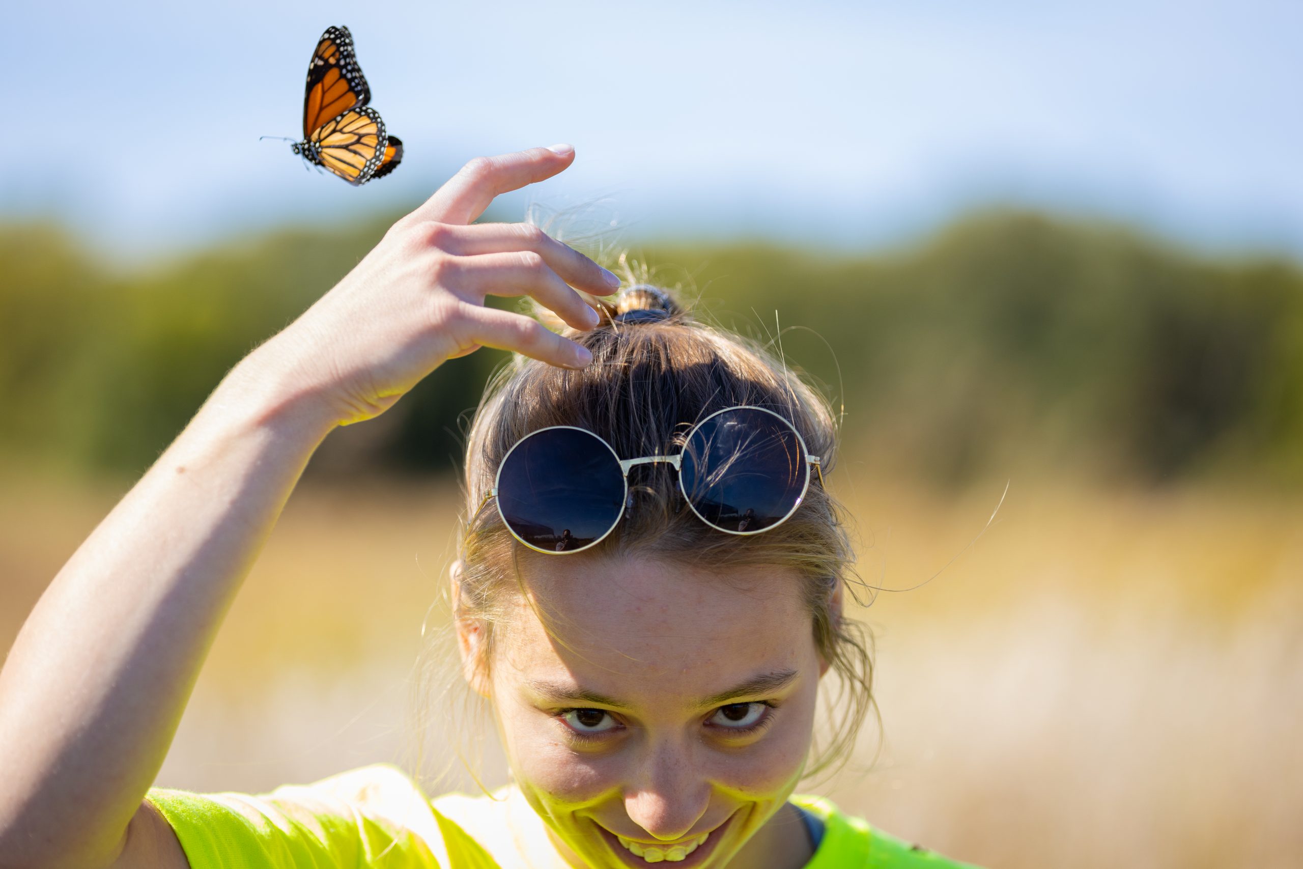 student smiling as a butterfly flies off of their hand that is over their head