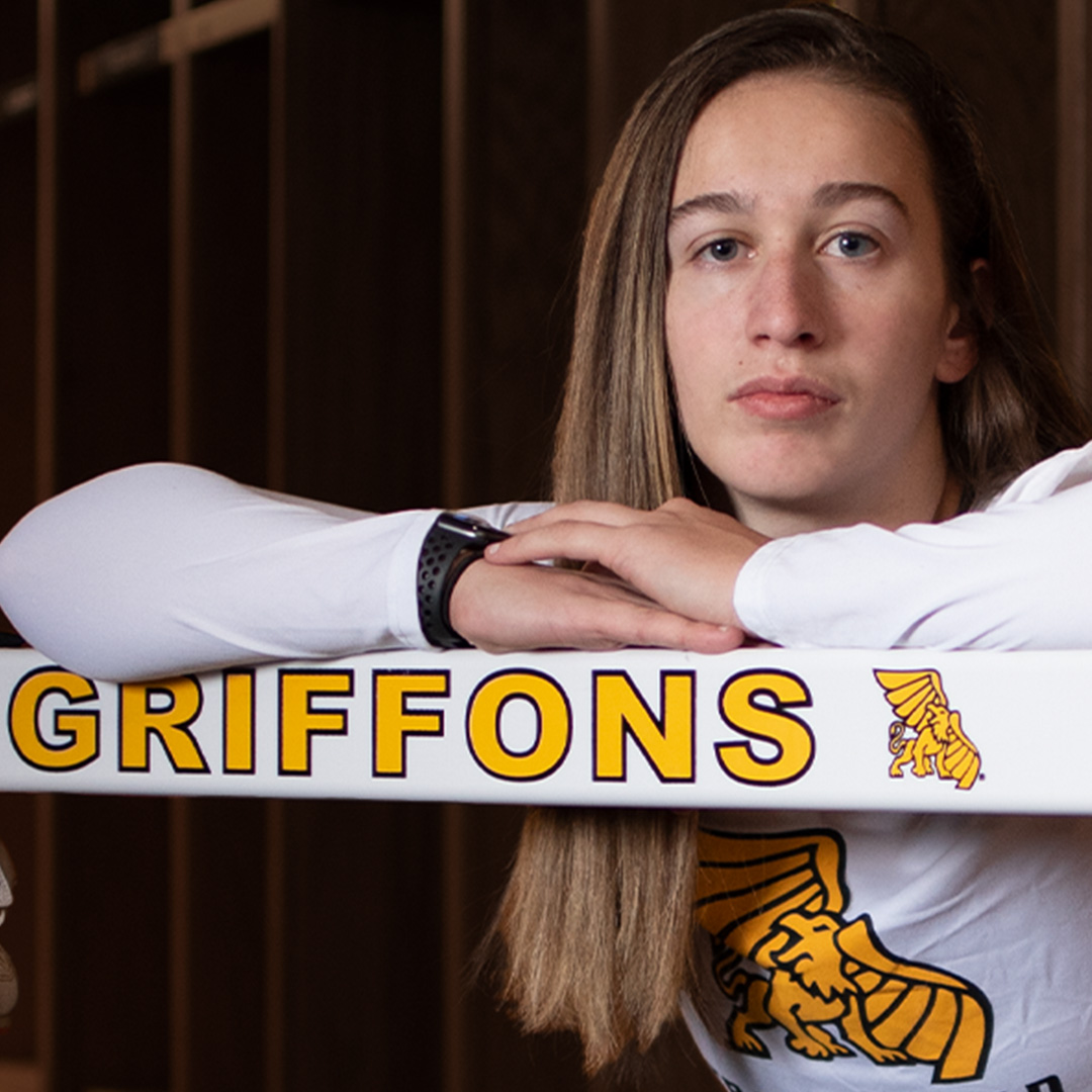 Bailey Gilbert posing for camera leaning on a hurdle reading Griffons