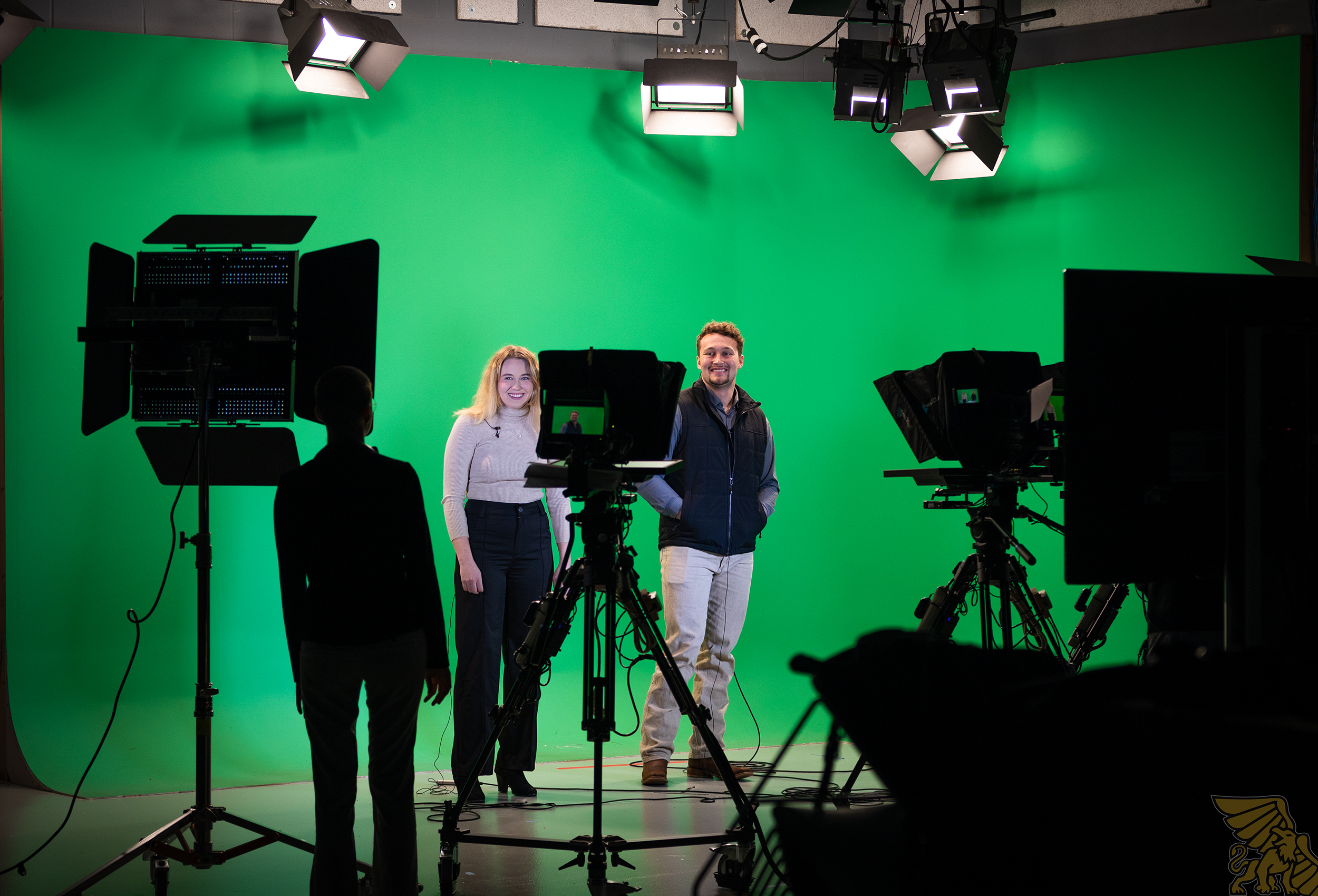 two students standing in front of a green screen surrounded by cameras