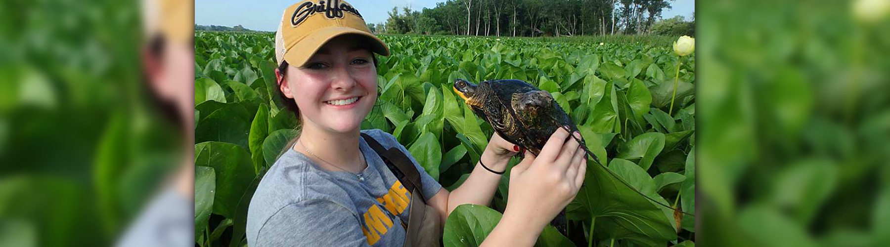 Student standing in field holding turtle