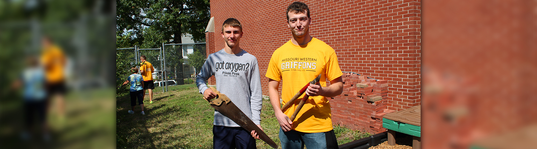 two students standing with tools ready to volunteer their services