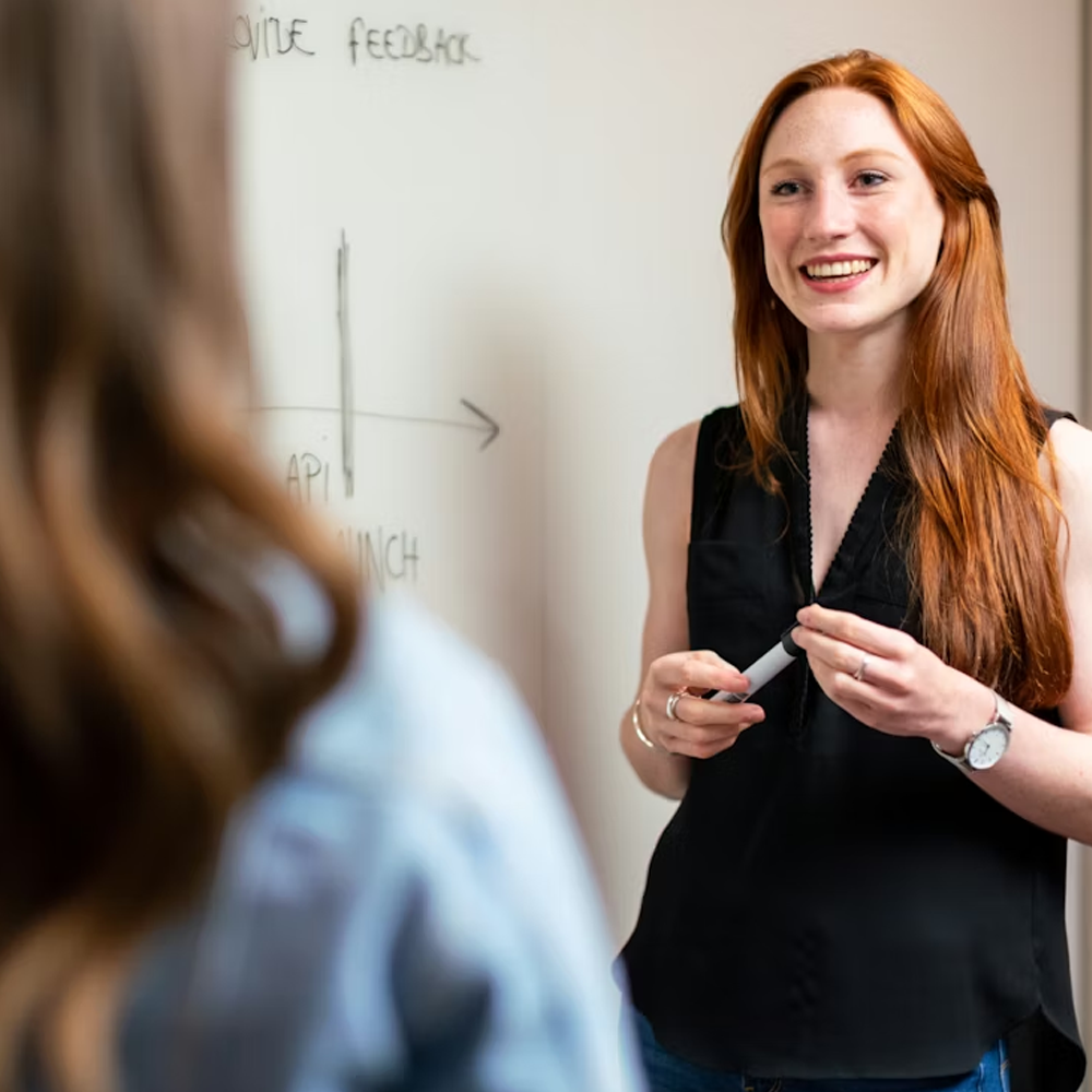 MeDSquare A teacher stands at a whiteboard smiling as she helps a student.