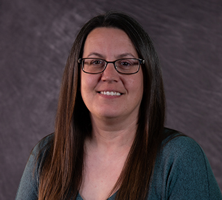 A woman with brown hair, glasses and a blue shirt smiles for the camera.
