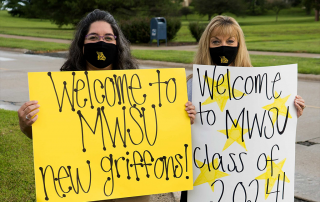 Two students wearing masks holding welcome signs