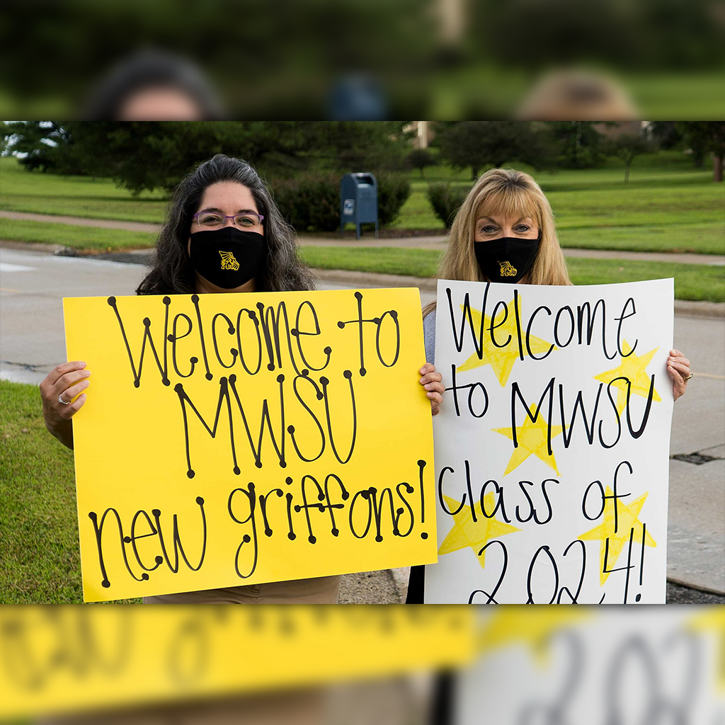 Two students wearing masks holding welcome signs