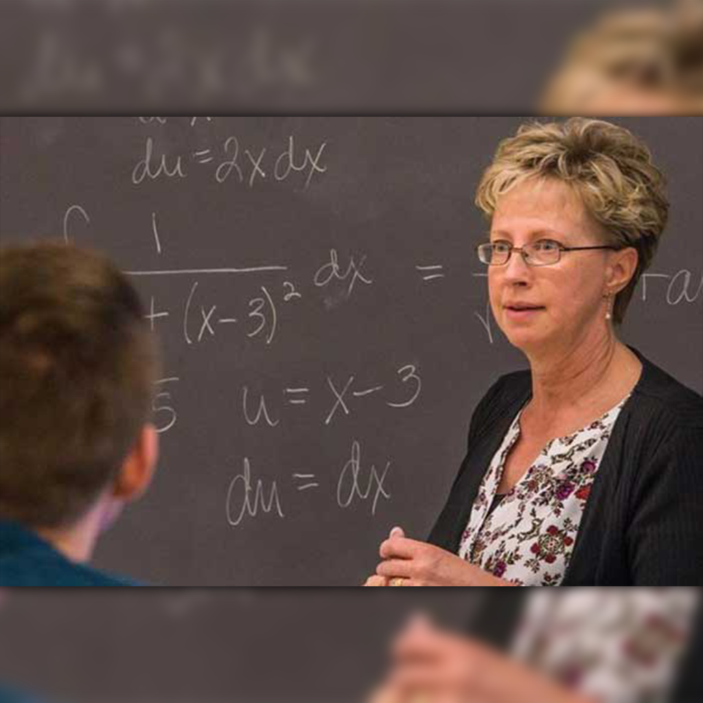 professor instructing a class with math equations on a chalk board in the background
