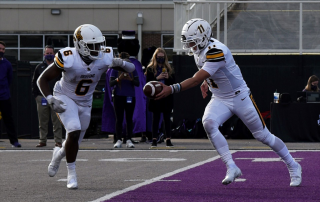 two college football players making a pass with a crowd watching