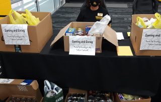 Kim Sigrist sits at a table behind several boxes of donated food.