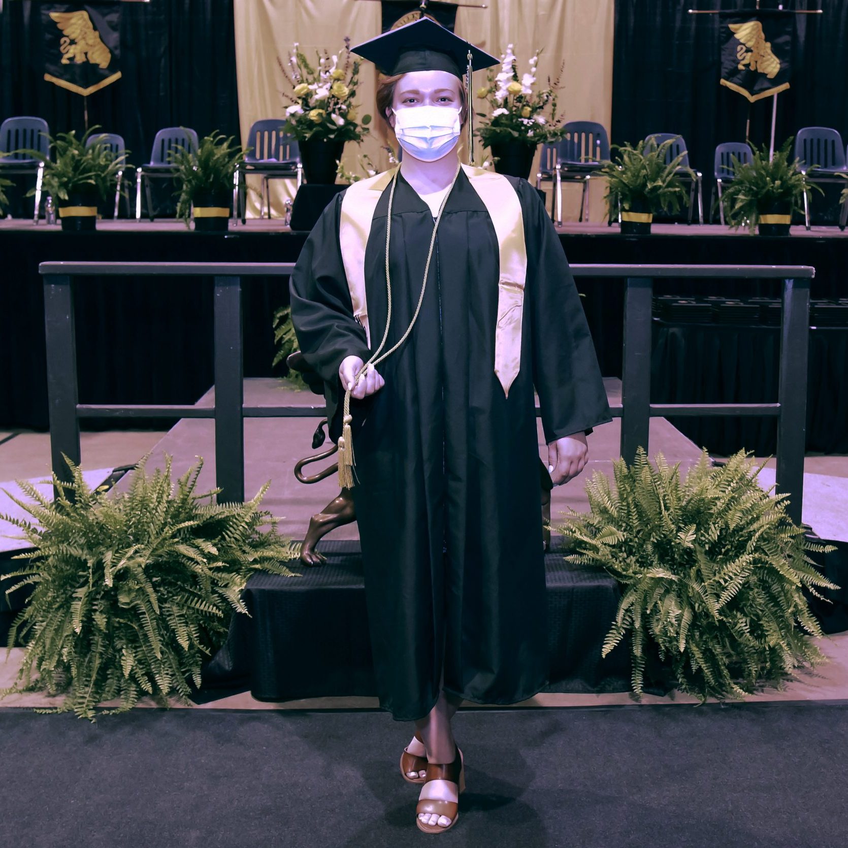 Allison Hildebrand posing for a photo in her cap and gown with commencement stage in background