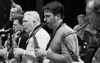 four saxophone players perform with a rhythm section in the background