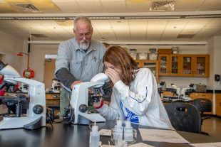 professor helping student at microscope