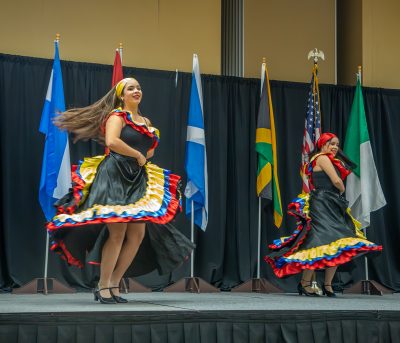 dancers in traditional dress on stage in front of international flags