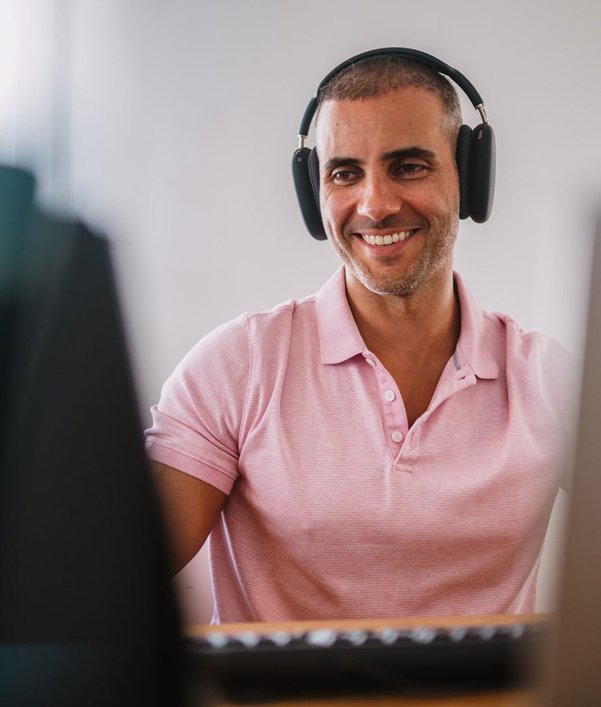 Man in pink polo with headphones at a computer