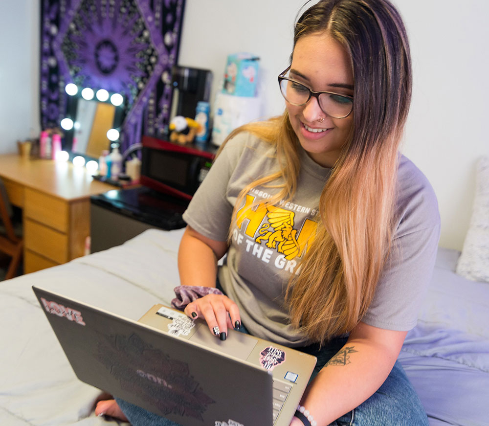 Student sitting on bed at home with laptop