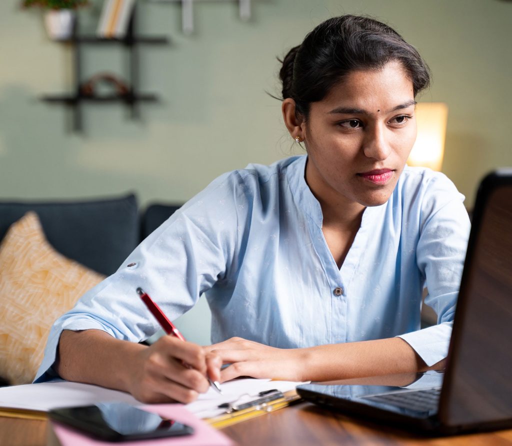Person taking notes while using a laptop at home