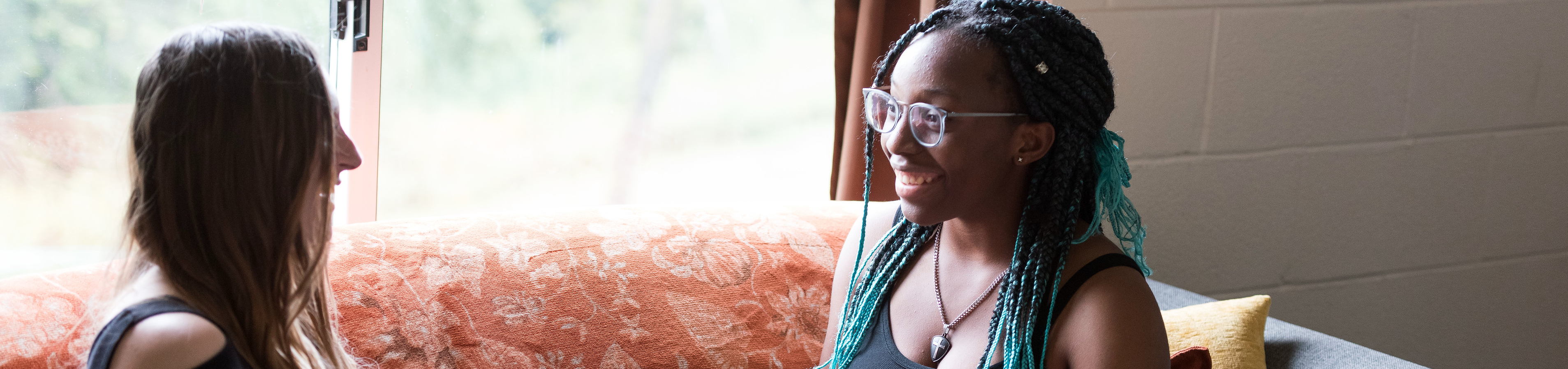 Two students smiling as they hang out in a residence hall.