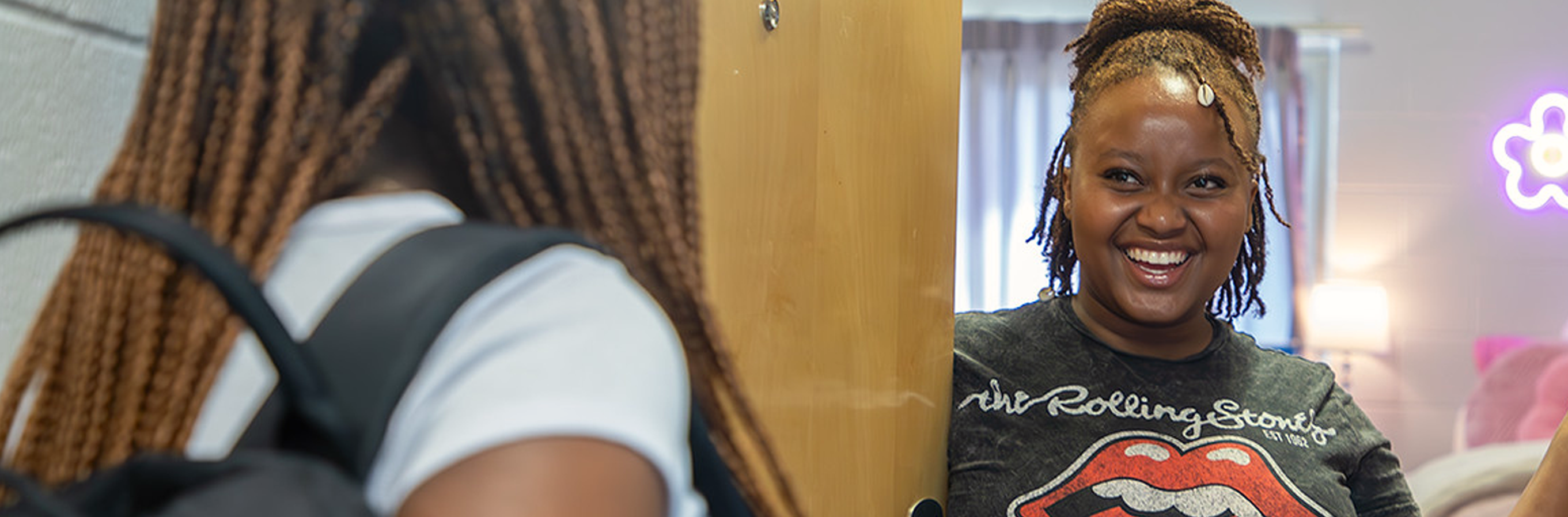 SmilingStudentsResidentialHall-Mobile Four students sit before a window on campus having a conversation.