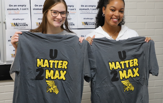 two students holding up u matter 2 max tshirts