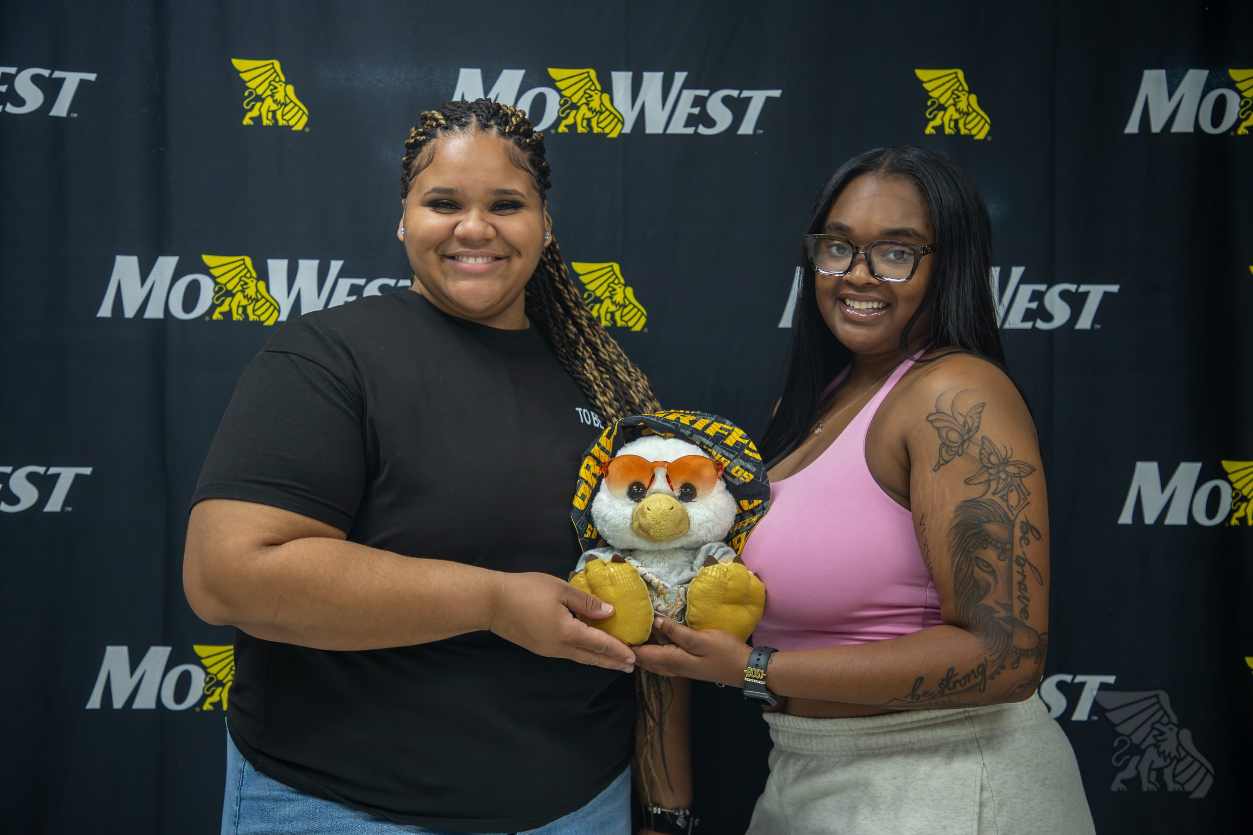 Two students smile as they hold little max wearing a black and gold bonnet.