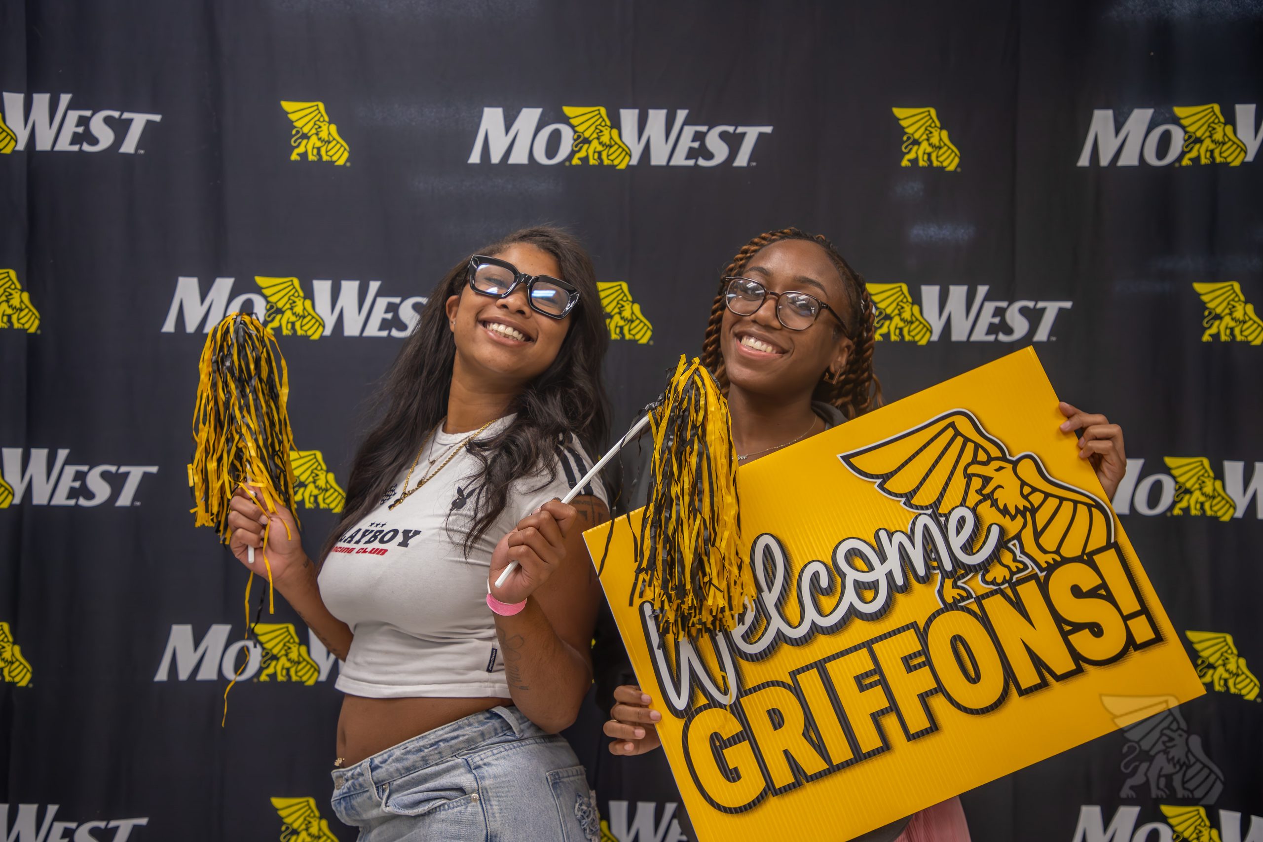 Students Smile Holding Gold and Black Pom Poms and a Gold Sign that says Welcome Griffons