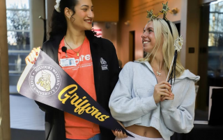 Two people stand looking at each other smiling holding MoWest Swag