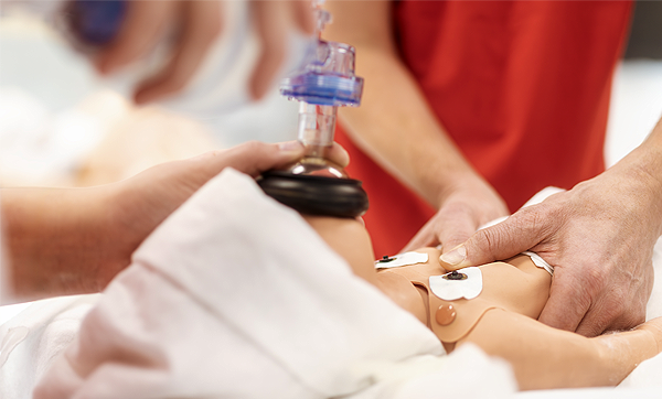 Adults perform CPR on a newborn simulation dummy.