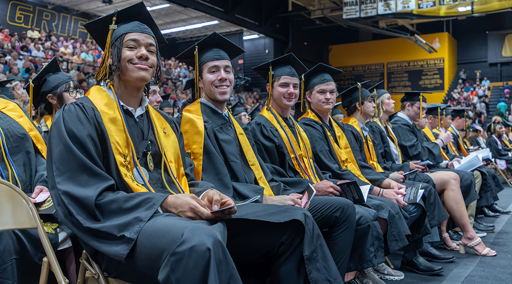 Student sitting in chairs at graduation in caps and gowns