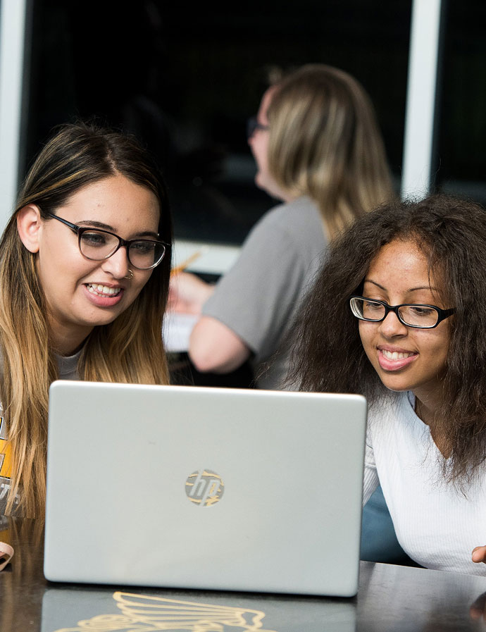 Students sharing a laptop at a campus table