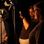 Autumn Moore blocks the light from the reflector from her eyes. The Motion Picture Lighting class continues to adjust the tools provided to see the different effects.